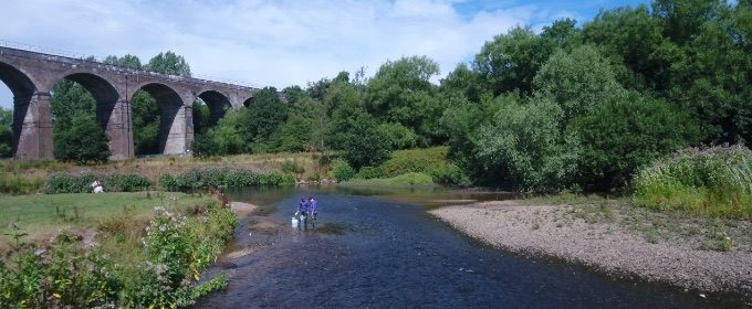 Two researchers collecting river bed samples