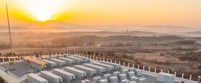 Battery storage compound within an arid environment in the foreground with an orange sunset in the background.