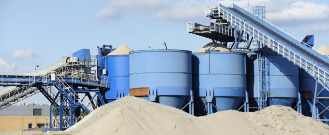Industrial blue containers in background with large piles of sand in front.