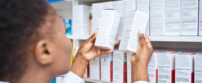 Back view of a female pharmacist standing in front of medicine shelves and holding medicine.